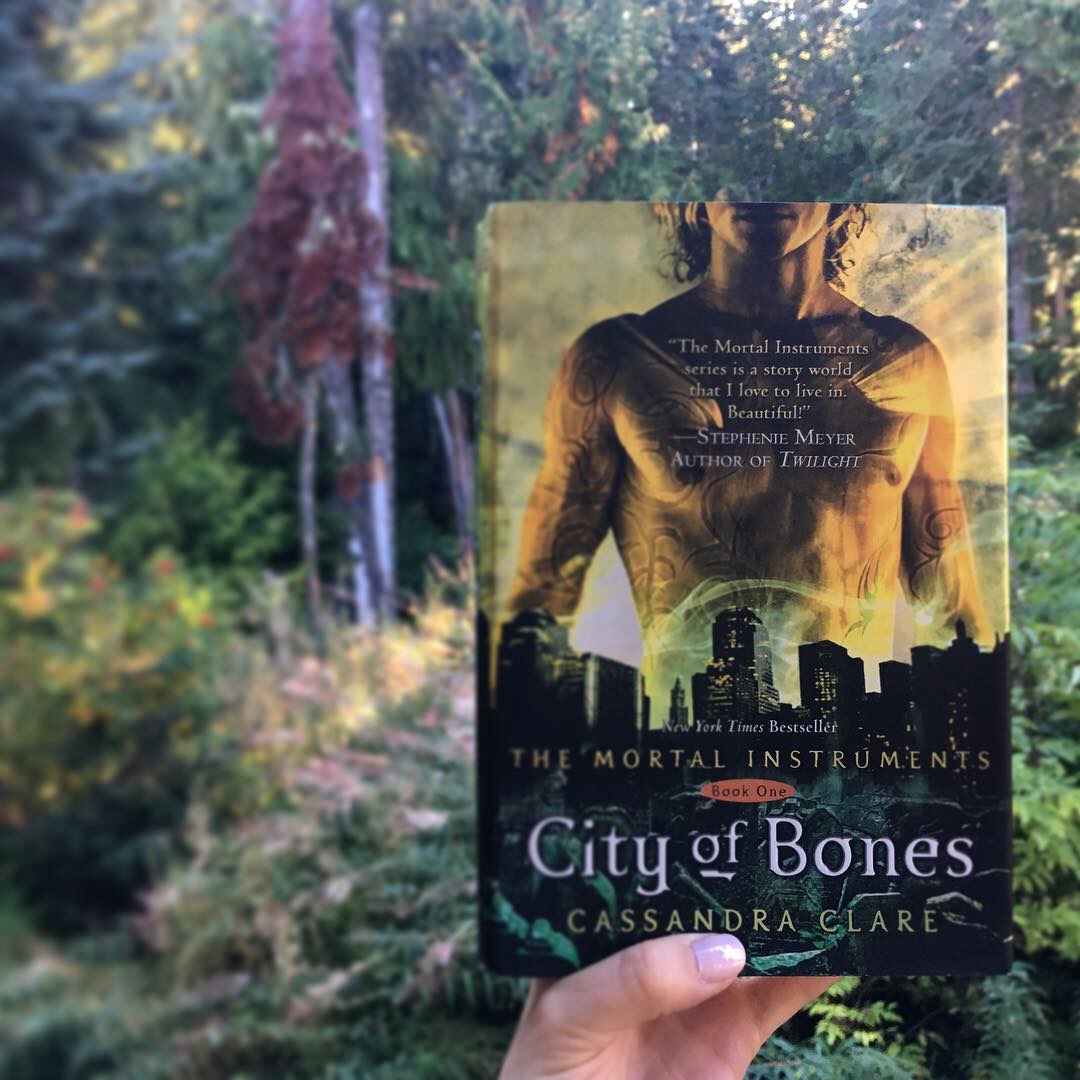 Hand holding hardcover edition of City of Bones against a backdrop of Pacific Northwest forest