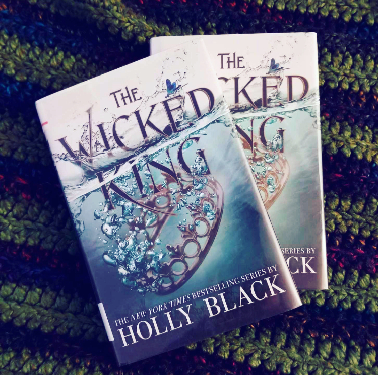 Two hardcover copies of the The WIcked King on top of a navy and green crocheted blanket