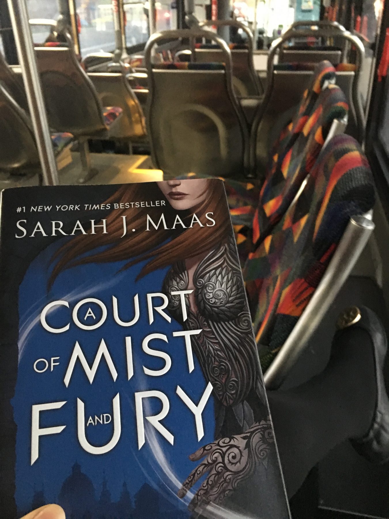 Hardcover copy of A Court of Mist and Fury with bus seats in the background