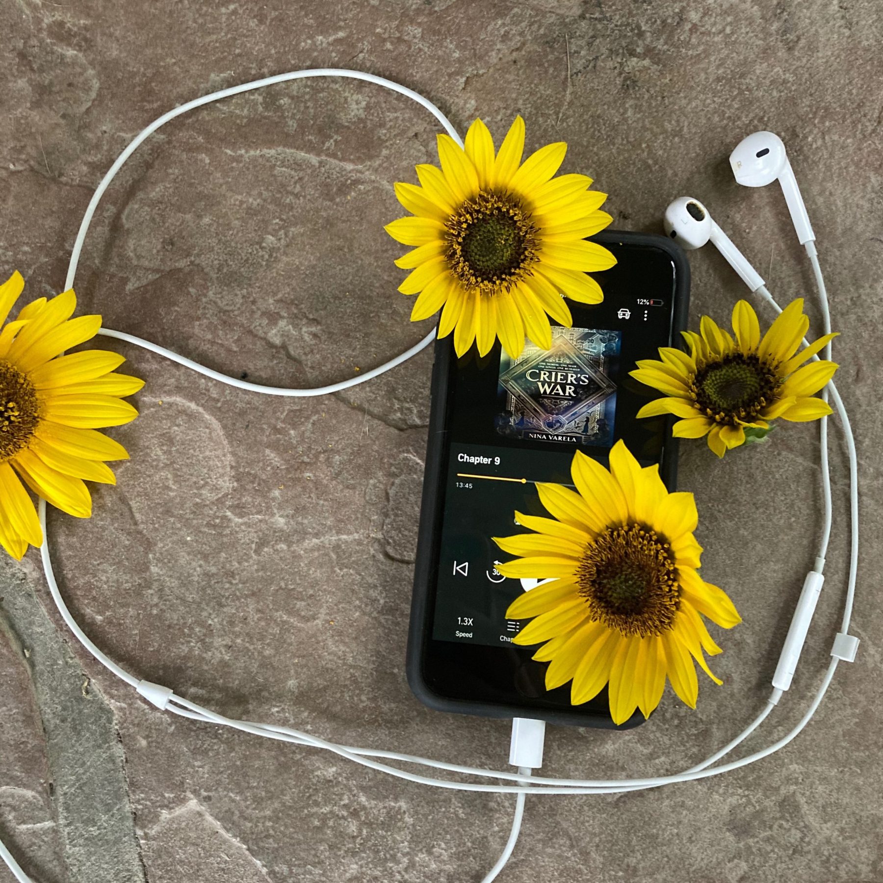 Crier's War audiobook pulled up on an iphone screen with sunflowers draped across the phone, and headphones surrounding the phone and flowers