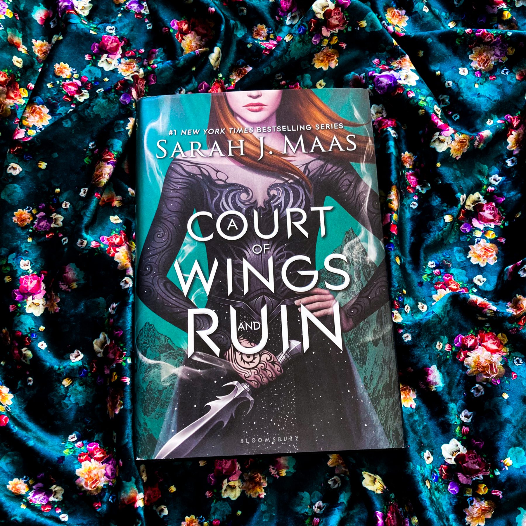 book, A Court of Wings and Ruin on a shiny blue-green floral scarf