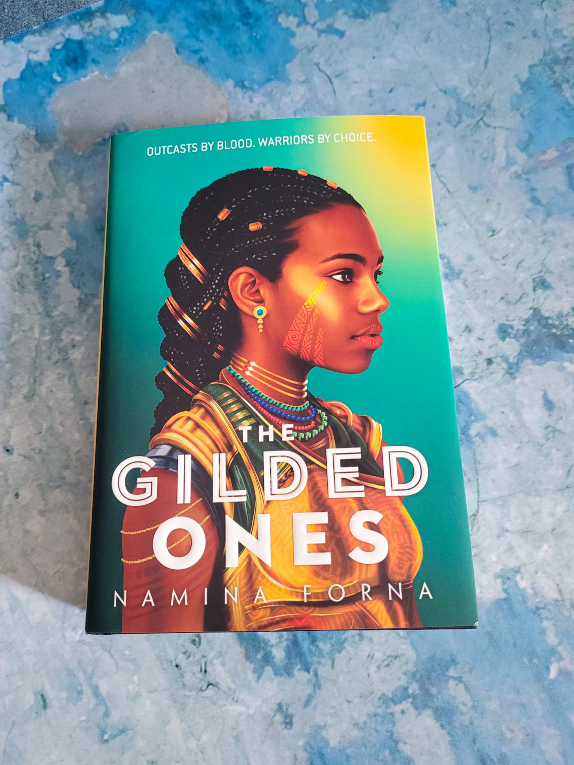 book, The Gilded Ones by Namina Forna on a blueish grey background