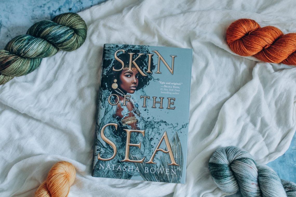 Skin of the Sea on a white cloth surrounded by orange, yellow, green, and light blue skeins of yarn.