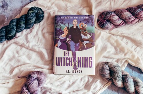 The Witch King on a white cloth surrounded by 4 blue, purple, and cream colored yarn skeins