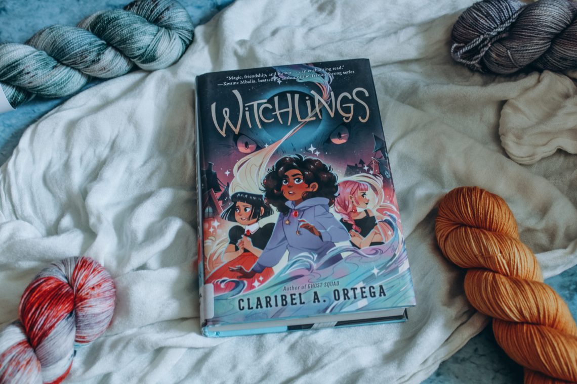 Witchlings on a white cloth surrounded by blue and orange skeins of yarn