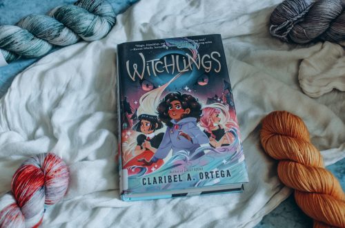Witchlings on a white cloth surrounded by blue and orange skeins of yarn