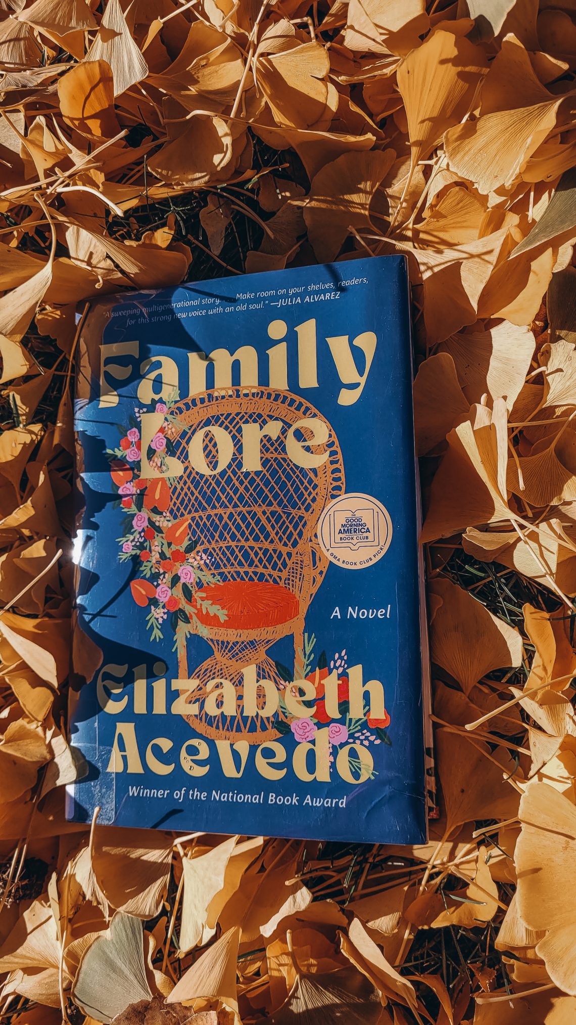 Hardcover copy of Family Lore by Elizabeth Acevedo in a pile of golden leaves